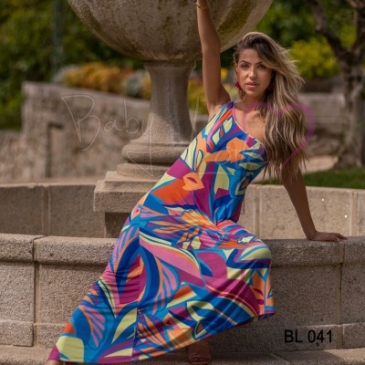 Vestido longo colorido com padrão abstrato, usado ao ar livre perto de fonte de pedra