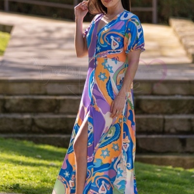 Mulher a usar vestido longo colorido, sandálias bege e óculos de sol brancos ao ar livre