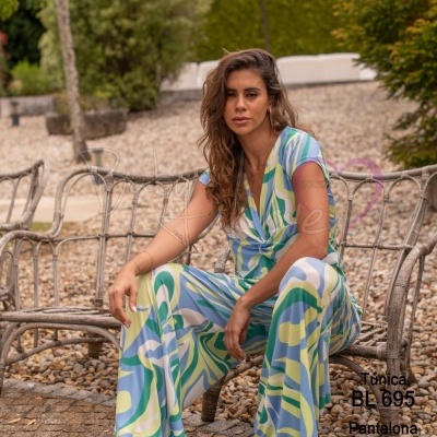 Conjunto túnica e pantalona com padrão abstrato azul, verde, branco e amarelo em modelo sentado em banco exterior