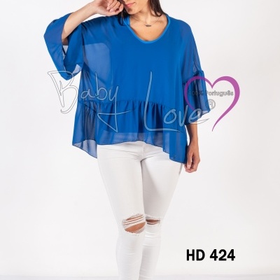 Mulher com blusa azul transparente de manga ampla, calças brancas rasgadas e botas azuis em fundo branco