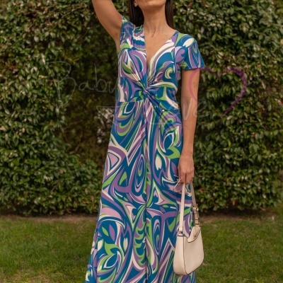 Vestido comprido com padrão abstrato em tons de azul, verde e lilás, com decote em V e nó frontal, modelo feminino a segurar mala branca.