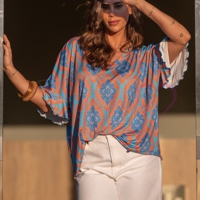 T-shirt feminina azul e laranja com calças brancas e pulseiras, modelo a proteger os olhos da luz