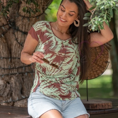 T-shirt feminina com padrão folhas verdes e castanhas, calções de ganga e óculos, sentada num banco de madeira ao ar livre