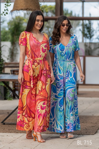 Duas mulheres com vestidos longos florais coloridos, um em tons quentes e outro em tons frios, num ambiente interior com luz natural