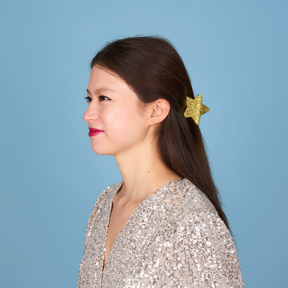 Mulher com grampo de cabelo dourado em forma de estrela e camisa prateada com lantejoulas