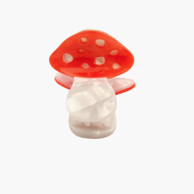Prendedor de cabelo em plástico em forma de cogumelo vermelho com manchas brancas.