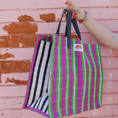 Saco de tecido colorido às riscas segurado por mão feminina junto a parede rosa