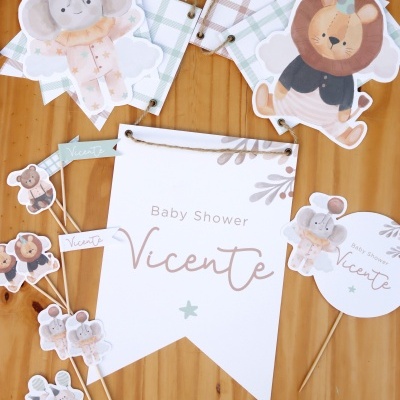 Cartaz e bandeirolas Baby Shower Vicente com ilustrações de elefante e leão sobre mesa de madeira