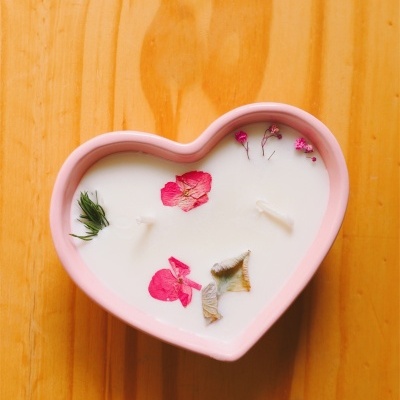 Vela decorativa em recipiente cor-de-rosa em forma de coração com flores secas