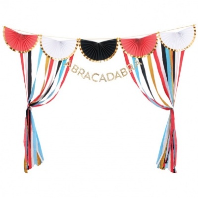 Decoração de festa com leques coloridos e faixa dourada 'ABRACADABRA'.