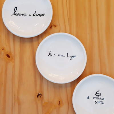 Pratos de cerâmica branca com frases em português sobre mesa de madeira