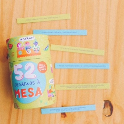 frasco cilíndrico colorido com texto e ilustrações, tiras de papel amarelas e azuis, superfície de madeira clara