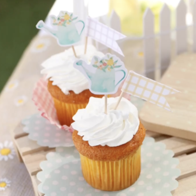 Dois cupcakes com cobertura branca e toppers decorativos em papel em cima de papel azul com bolinhas brancas