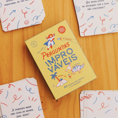 Conjunto de cartas de perguntas em português com caixa amarela e cartas espalhadas sobre mesa de madeira