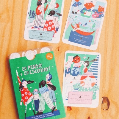 Jogo de cartas com embalagem verde e ilustrações coloridas sobre mesa de madeira