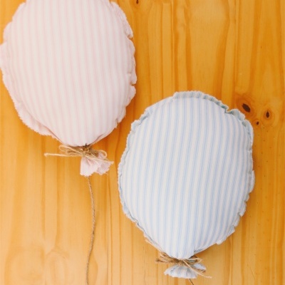 Almofadas em forma de balão rosa e azul com riscas penduradas em fundo de madeira clara