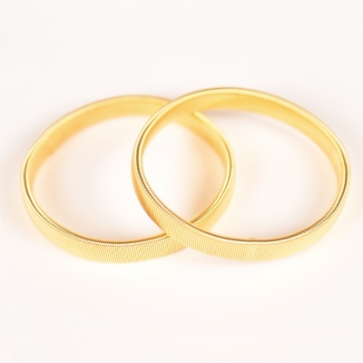 Dois braceletes dourados com textura fina sobre fundo branco