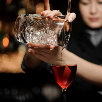 Copo de vidro com gelo a despejar líquido vermelho num copo de cocktail