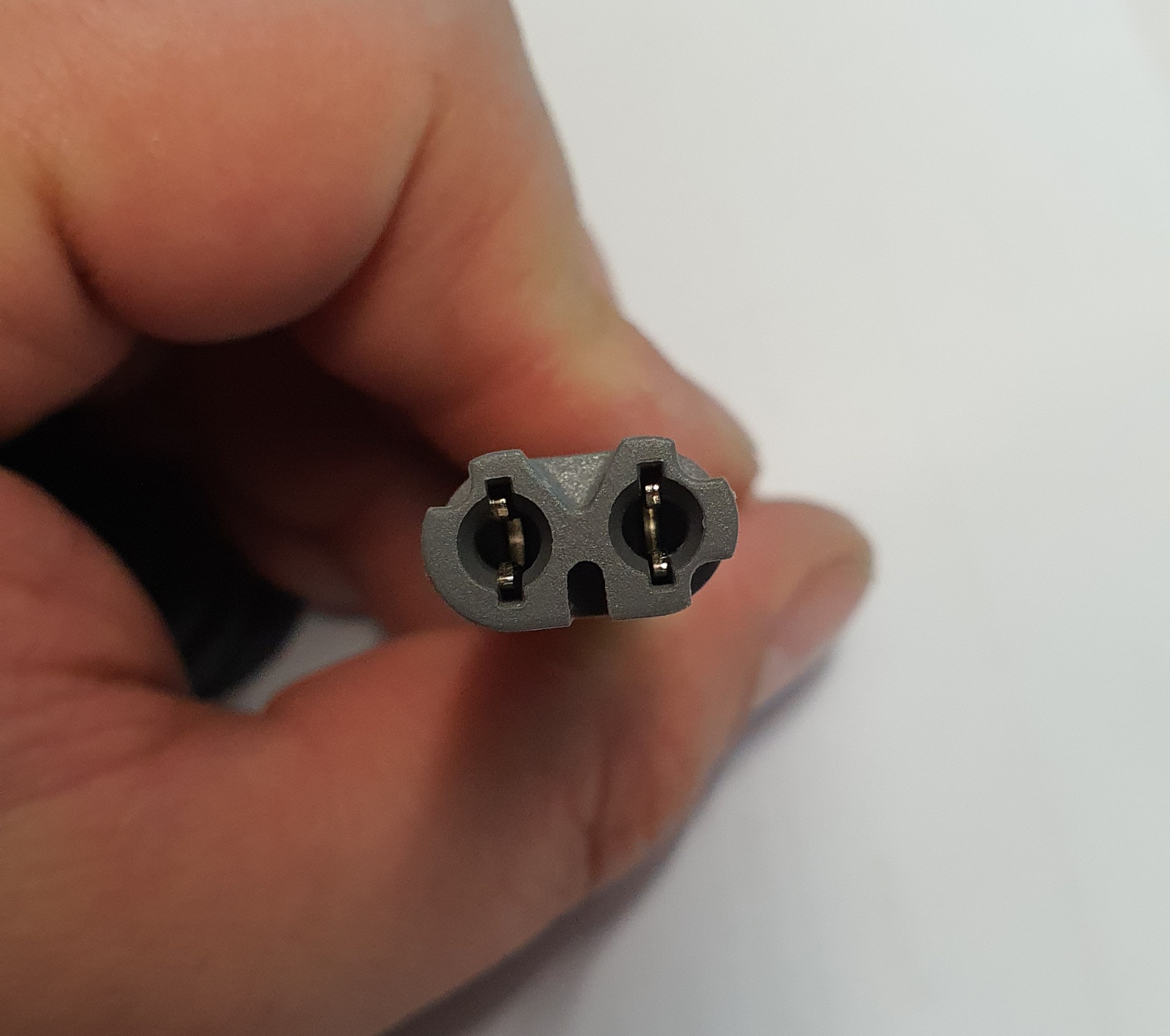 Cabo elétrico preto com conector duplo cinzento segurado por uma mão