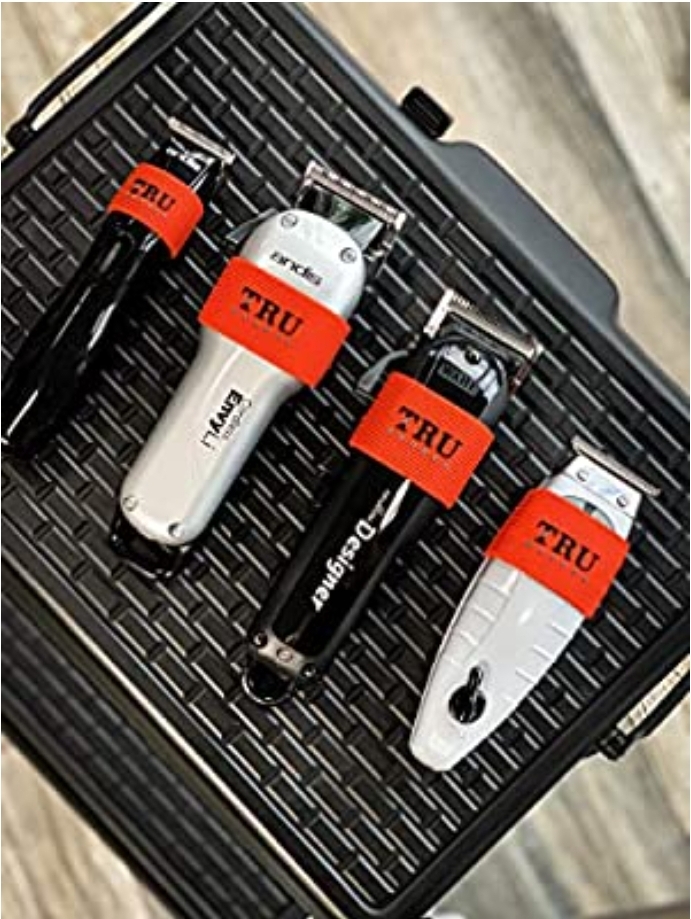 Quatro máquinas de cortar cabelo preta e branca com etiquetas vermelhas TRU sobre superfície preta texturizada.