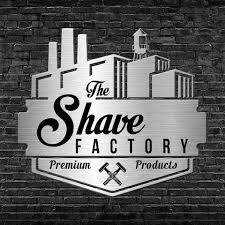 Logótipo metálico prateado com texto 'The Shave Factory' e 'Premium Products' sobre parede de tijolos