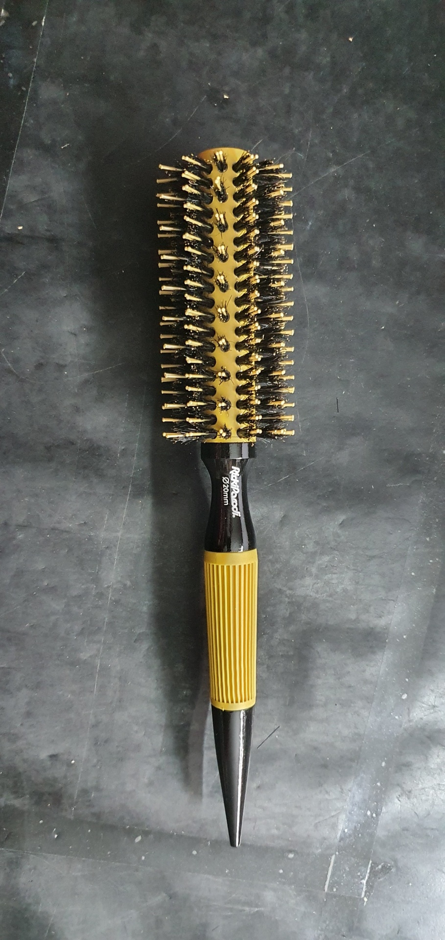 Escova de cabelo redonda com cerdas pretas e douradas e cabo preto e amarelo sobre superfície escura