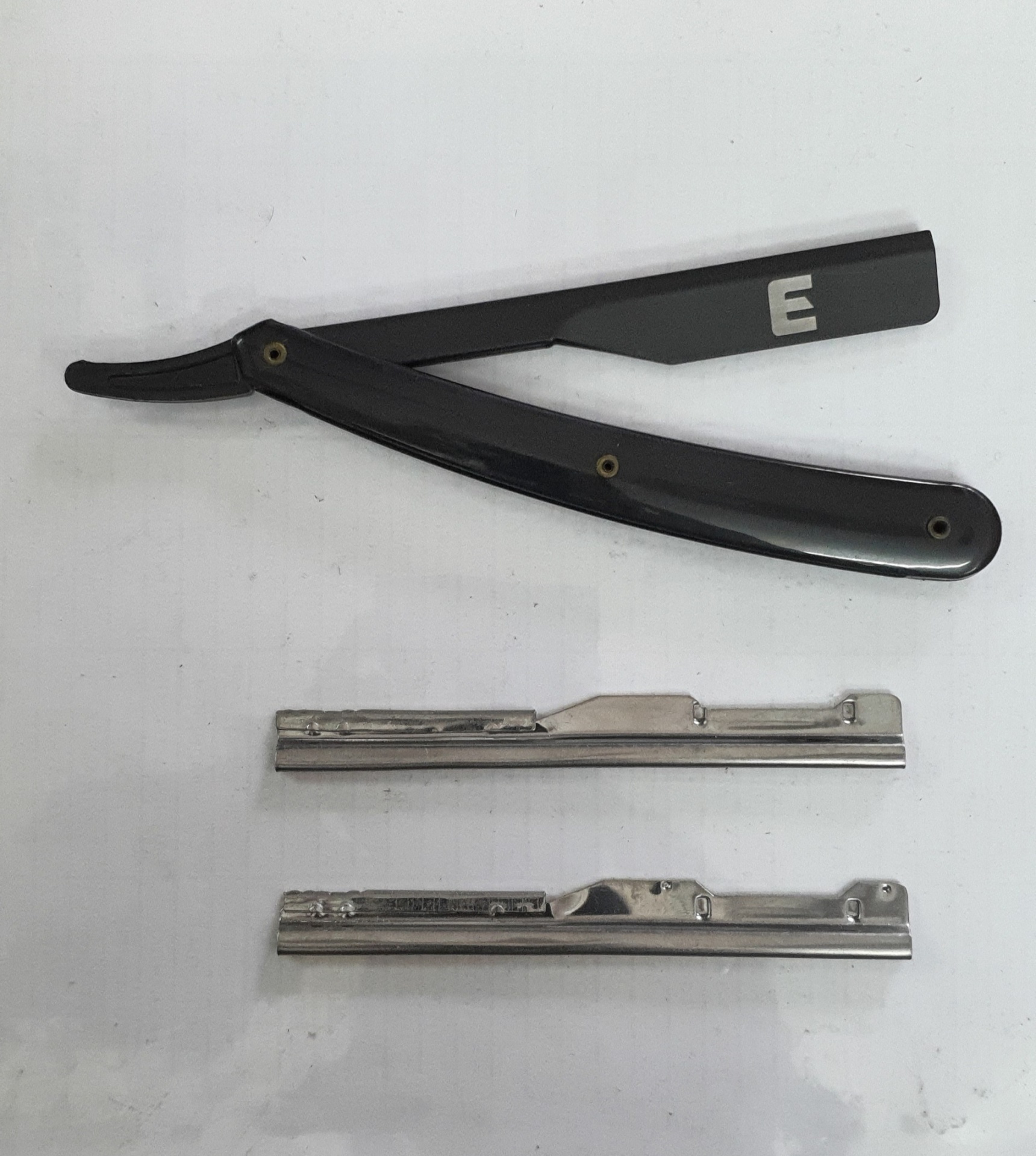 Navalha de barbear preta com letra E branca e duas peças metálicas prateadas