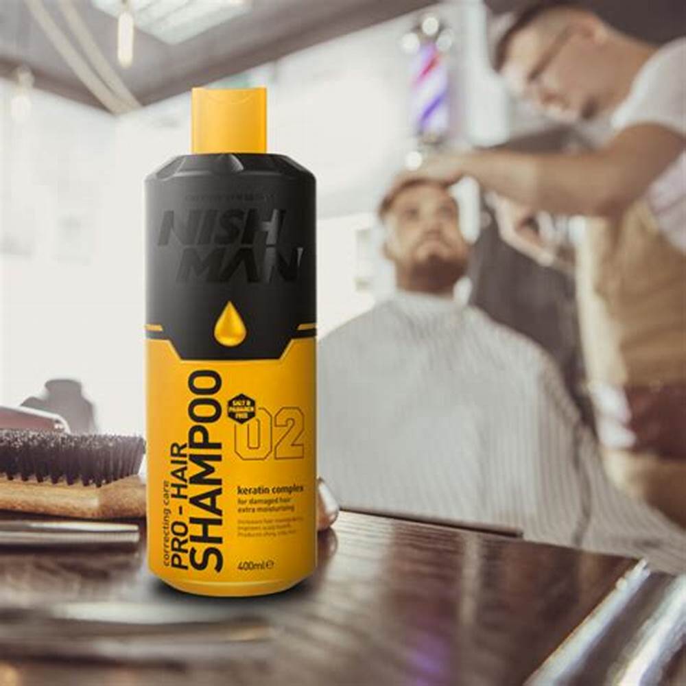 Frasco de champô preto e amarelo NISH MAN em mesa de barbearia com barbeiro a cortar cabelo ao fundo