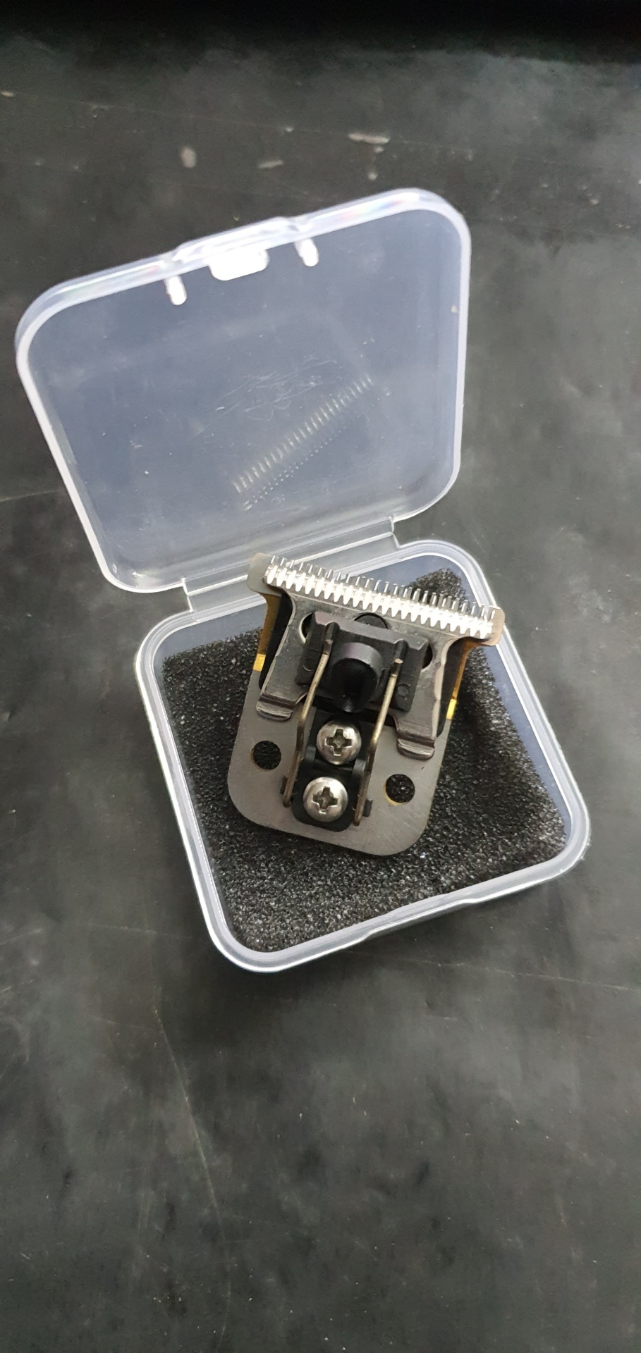 Cabeça de lâmina de máquina de cortar cabelo em caixa plástica transparente sobre superfície preta