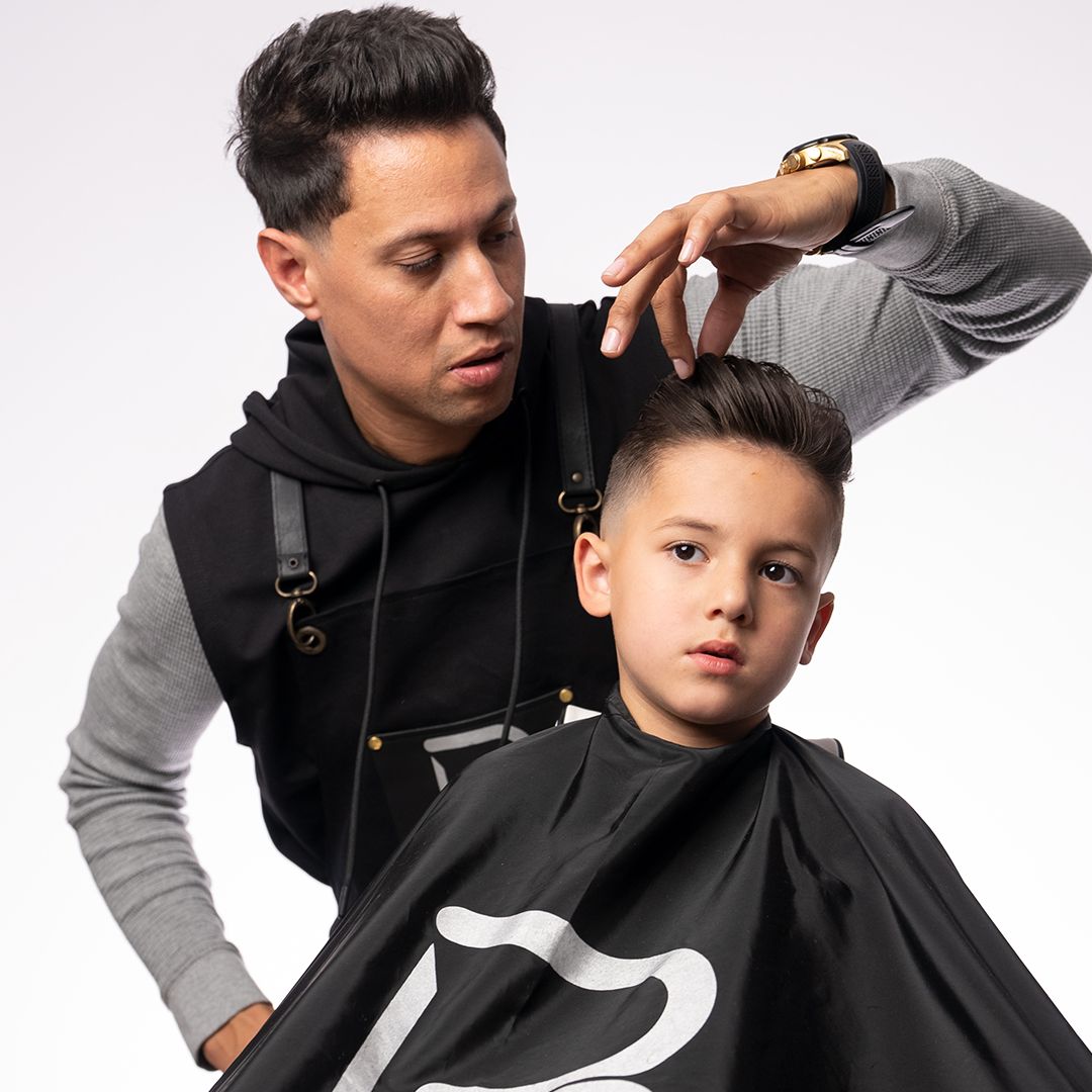 Barbeiro a cortar cabelo a um rapaz com capa preta