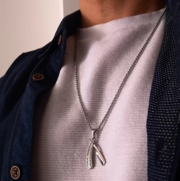 Colar prateado com pendentes em pescoço vestido com t-shirt branca e camisa azul escura