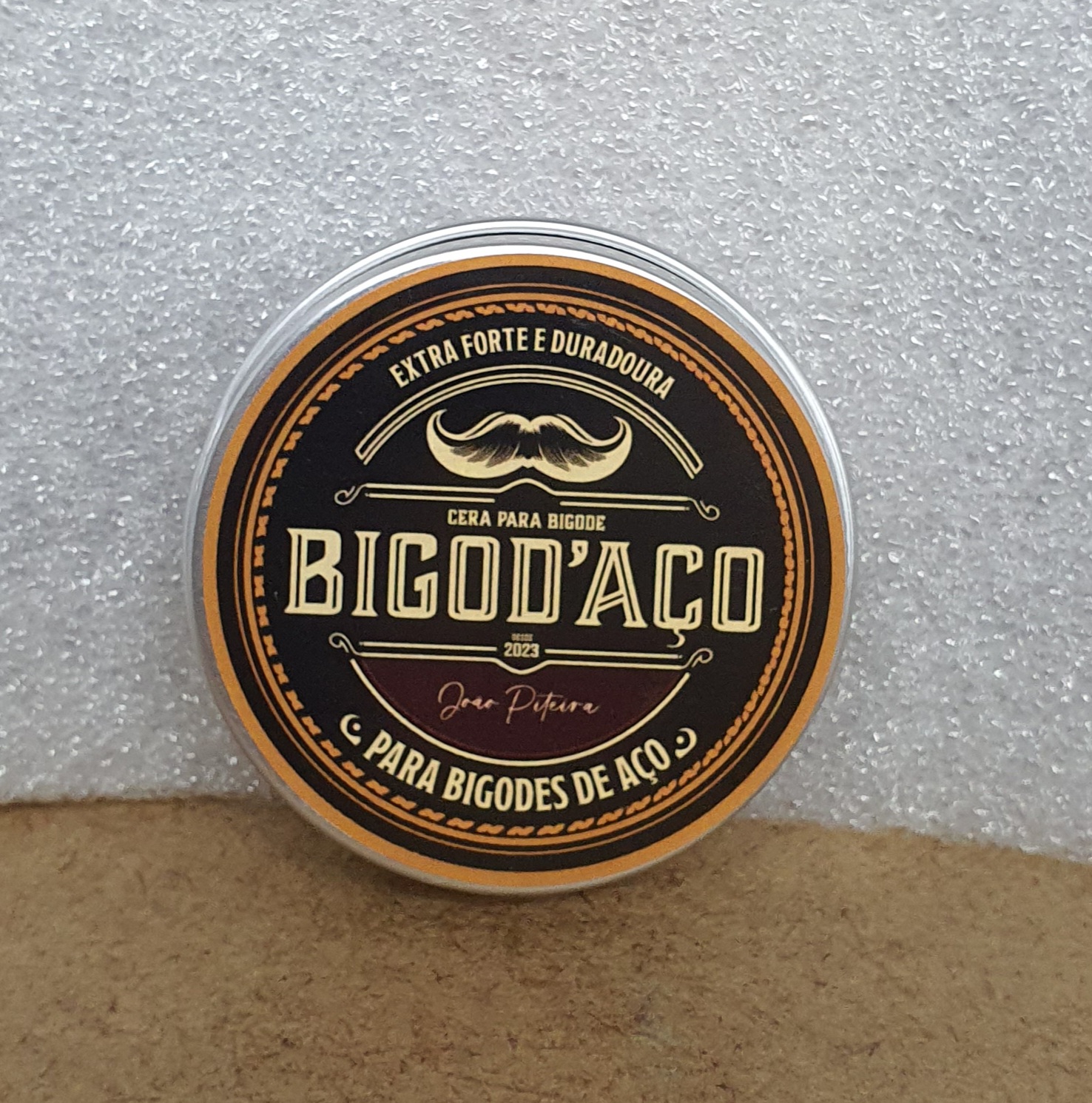 Pote redondo de cera para bigode com tampa preta e detalhes em laranja