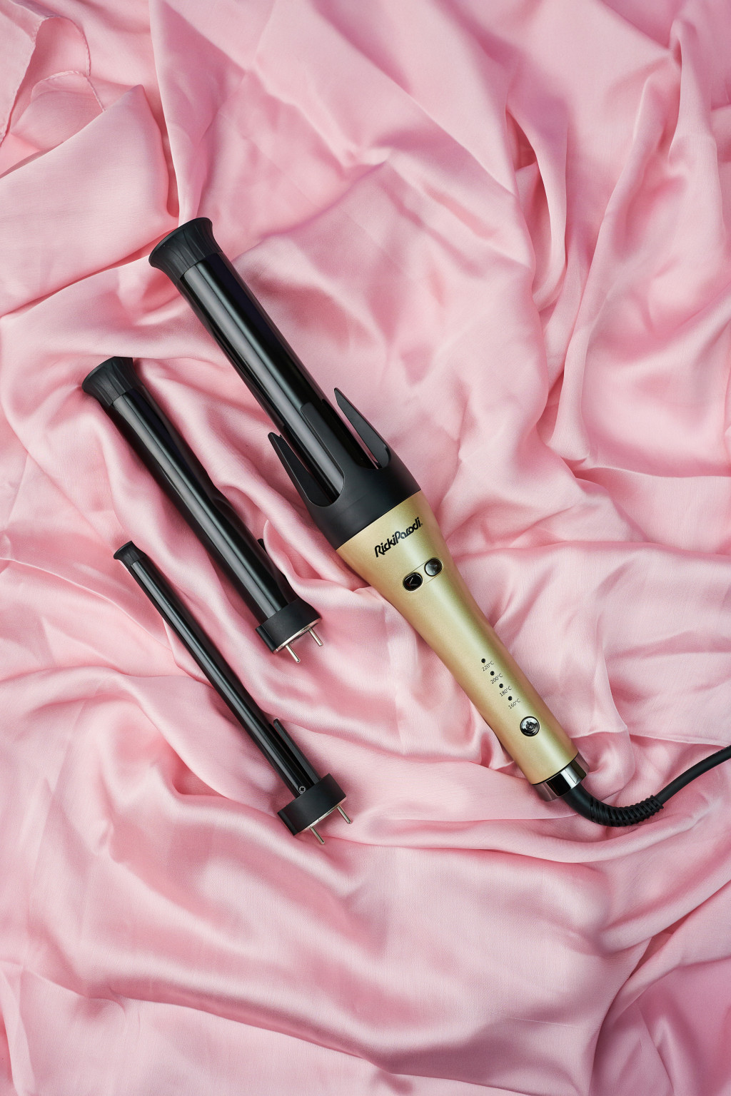 Conjunto de modelador de cabelo com três acessórios preto e dourado sobre tecido rosa