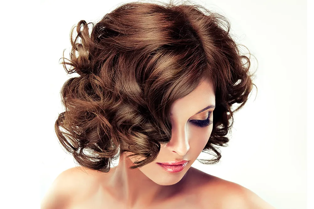 Mulher com cabelo castanho volumoso e ondulado, maquilhagem suave, fundo branco