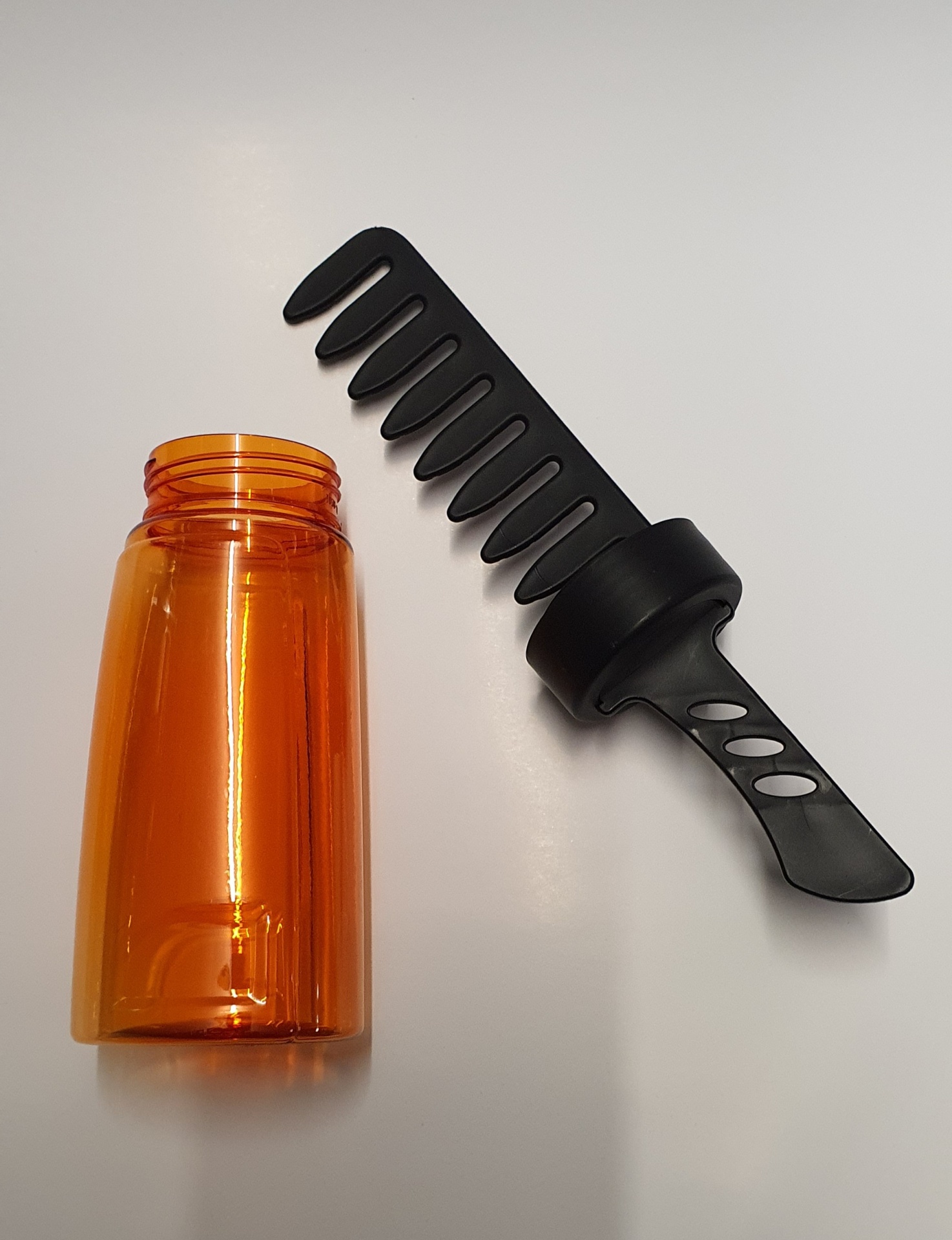 Frasco plástico laranja e aplicador preto com dentes largos