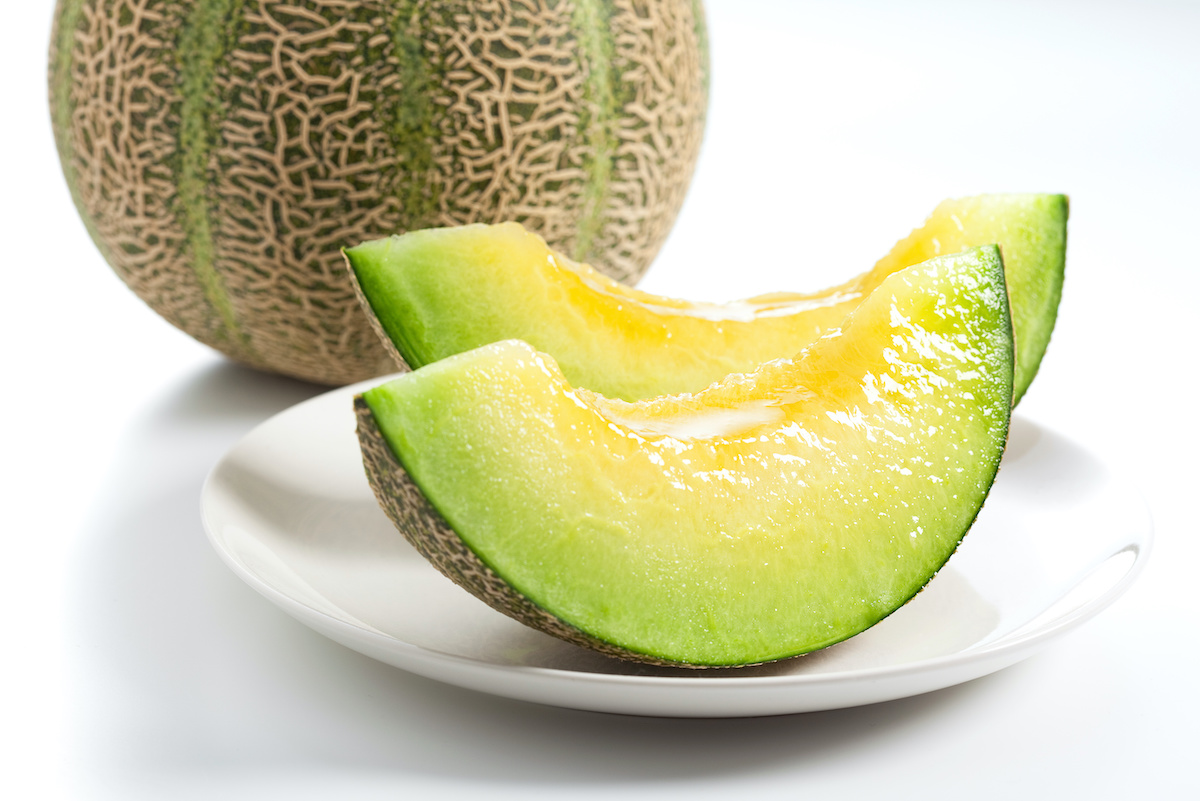 Fatias de melão verde e amarelo num prato branco com melão inteiro ao fundo