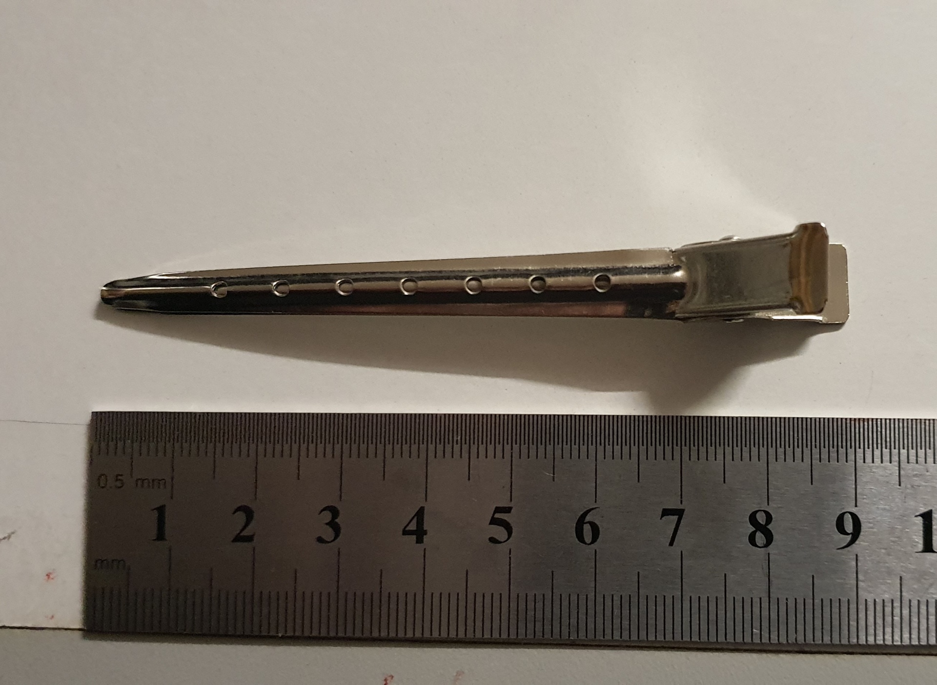 Clipe metálico prateado ao lado de régua metálica