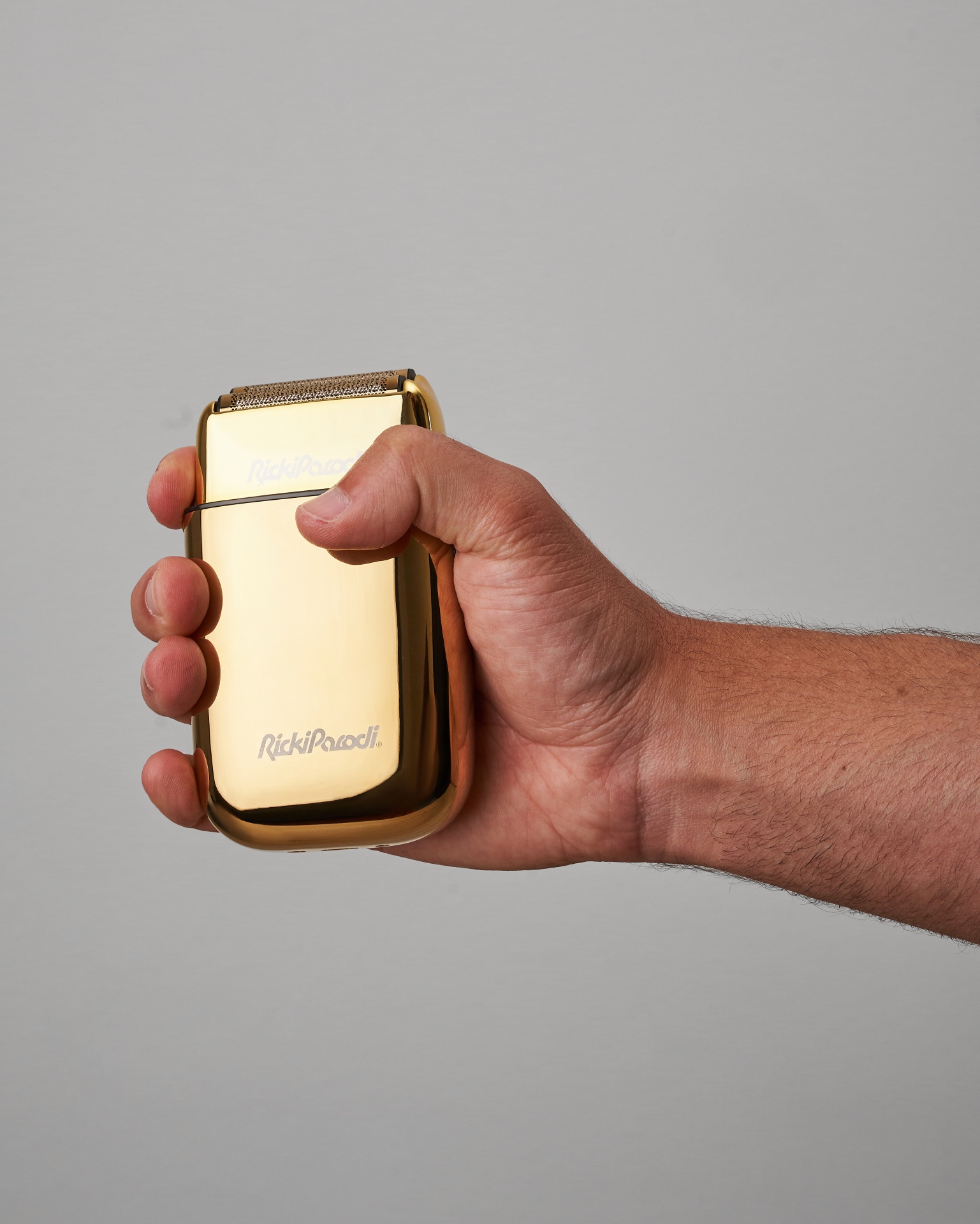 Aparelho de barbear elétrico dourado da marca RickiParodi numa mão masculina sobre fundo cinzento