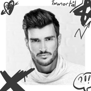Retrato em preto e branco de homem com suéter de gola alta branco e desenhos gráficos ao redor