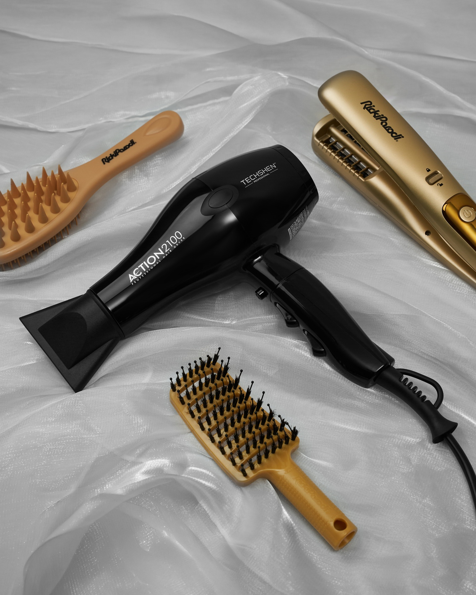 Secador de cabelo preto, penteados bege, alisador dourado sobre tecido branco