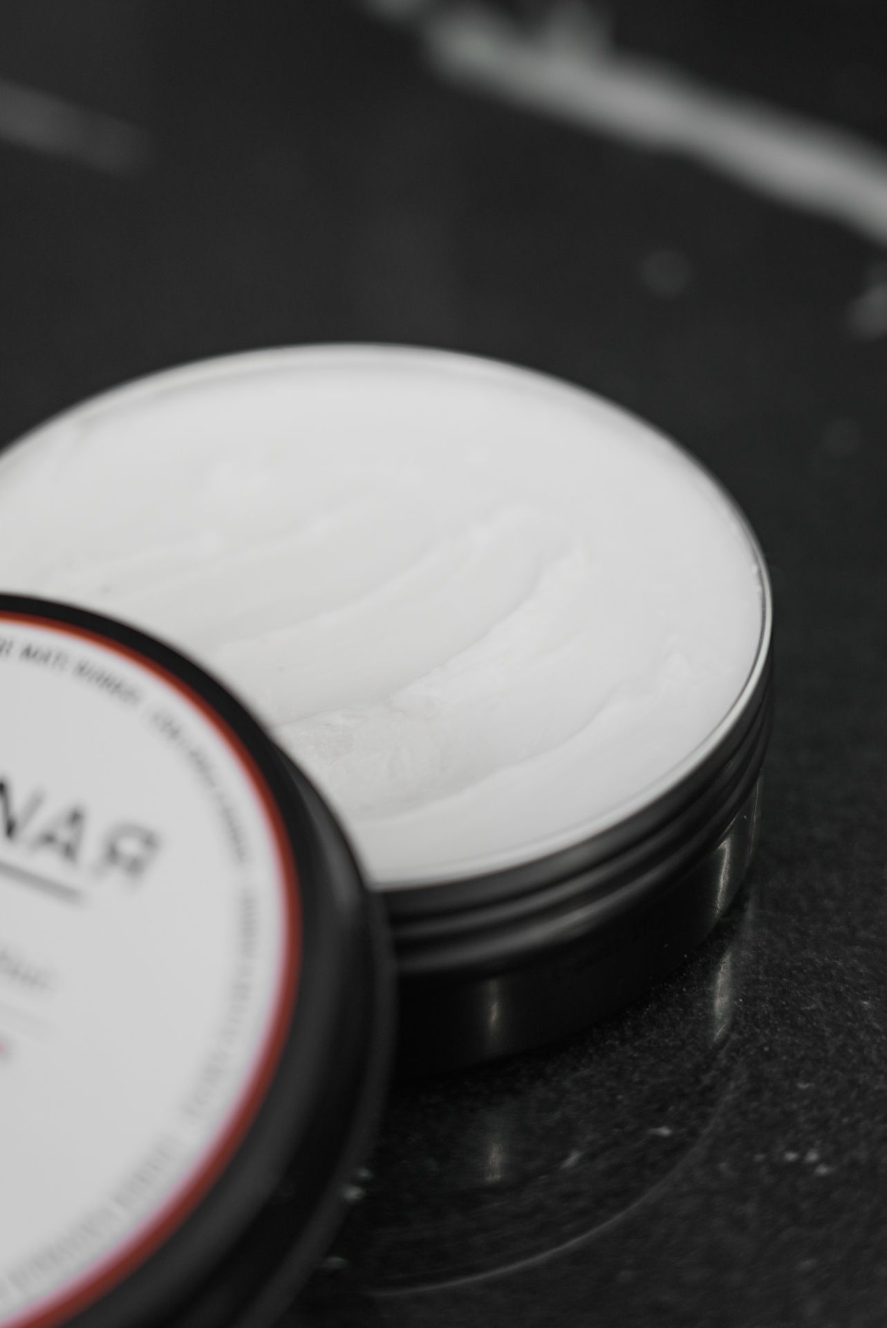 Pote preto aberto com creme branco em superfície escura