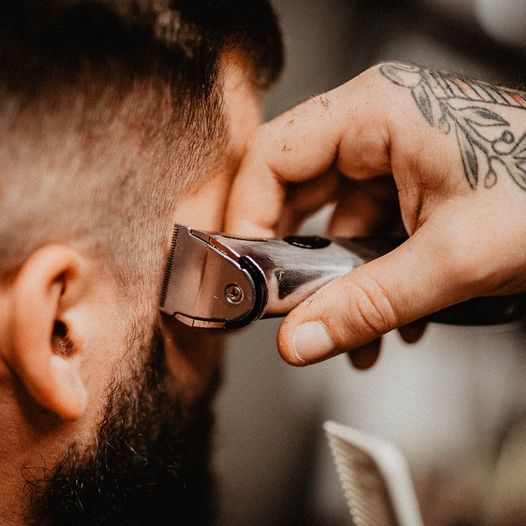 Máquina de cortar cabelo metálica usada para aparar cabelo castanho de homem com barba