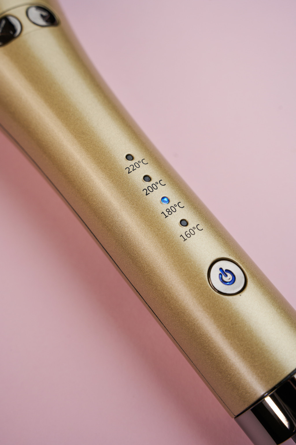 Dispositivo dourado com indicador de temperatura e botão azul num fundo rosa