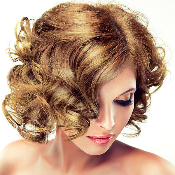 Mulher com cabelo ondulado castanho claro e maquilhagem contra fundo branco