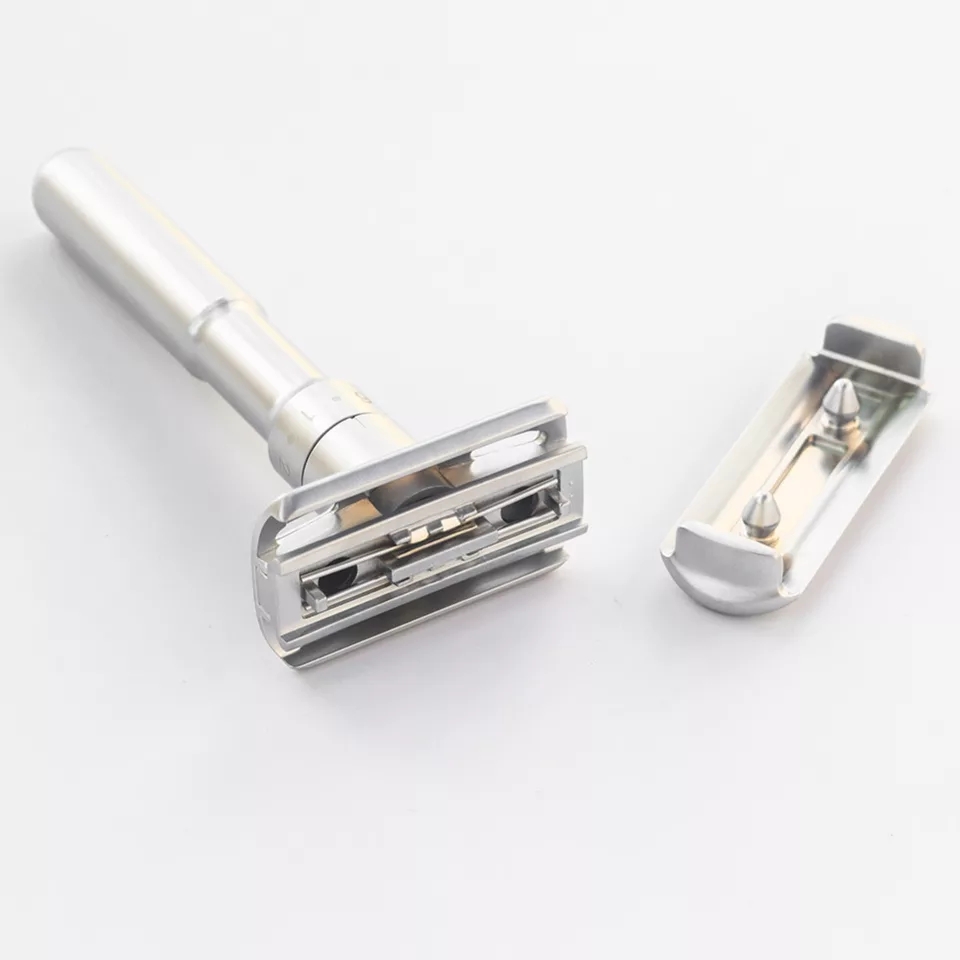 Navalha de barbear metálica prateada desmontada sobre fundo branco