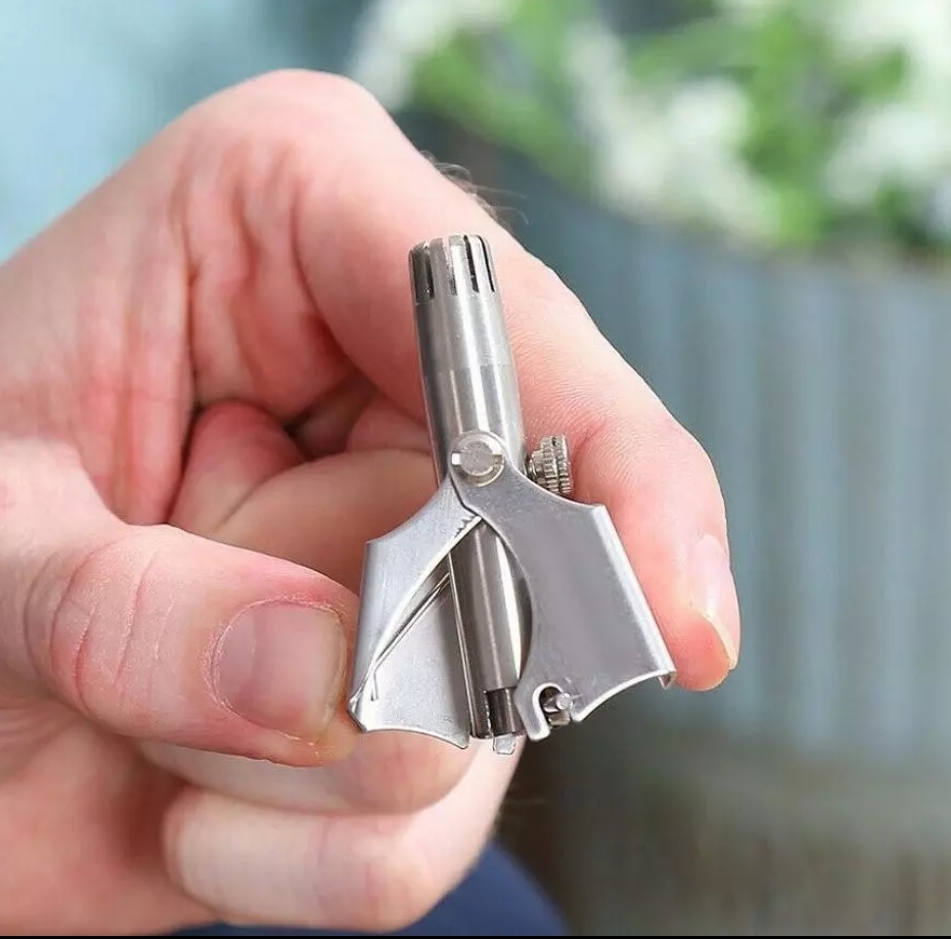 Ferramenta pequena prateada segurada por uma mão, fundo desfocado verde e cinzento