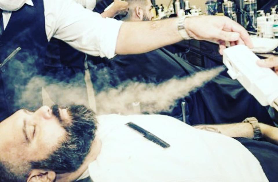 Homem com barba a receber vapor portátil numa barbearia.