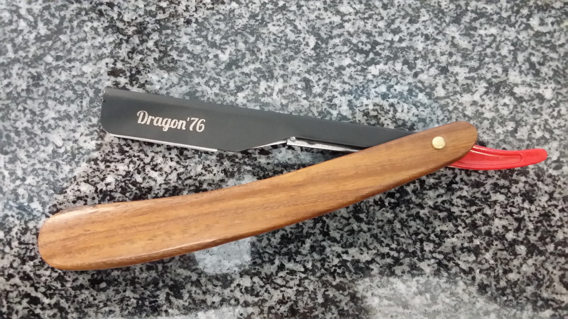 Navalha de barbear com lâmina preta e cabo de madeira clara sobre granito cinzento