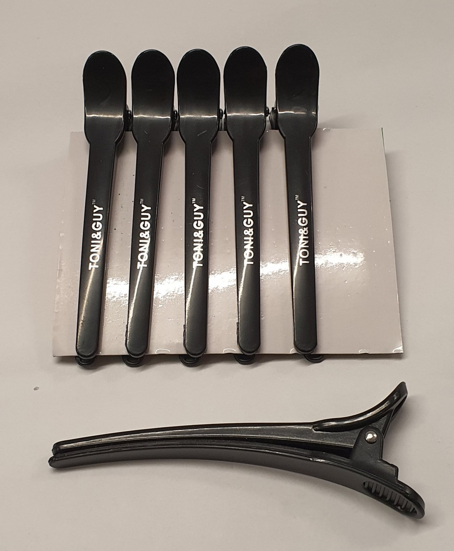Cinco colheres de plástico pretas com inscrição TONI&GUY e uma presilha de cabelo preta