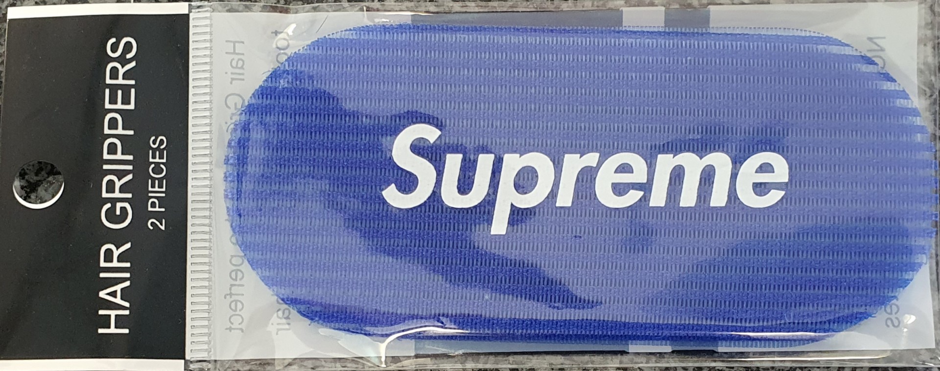 Conjunto de 2 grampos de cabelo azuis Supreme em embalagem transparente.